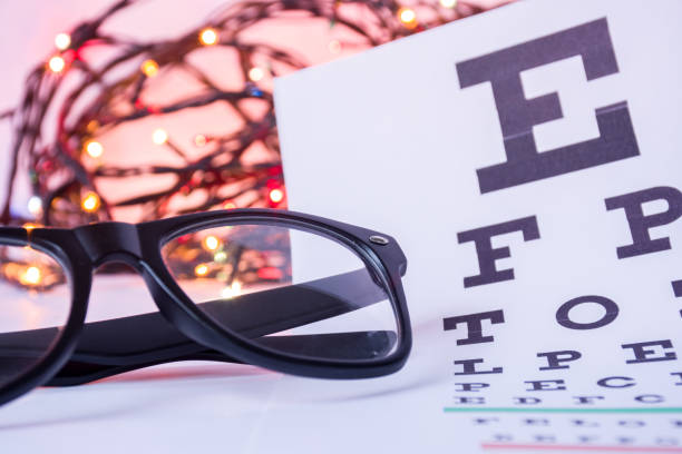 istock Christmas and New Year in ophthalmology optometry. Eyeglasses and ophthalmological table for visual acuity test in foreground with blurred lights bulbs Christmas garlands in background 893160604