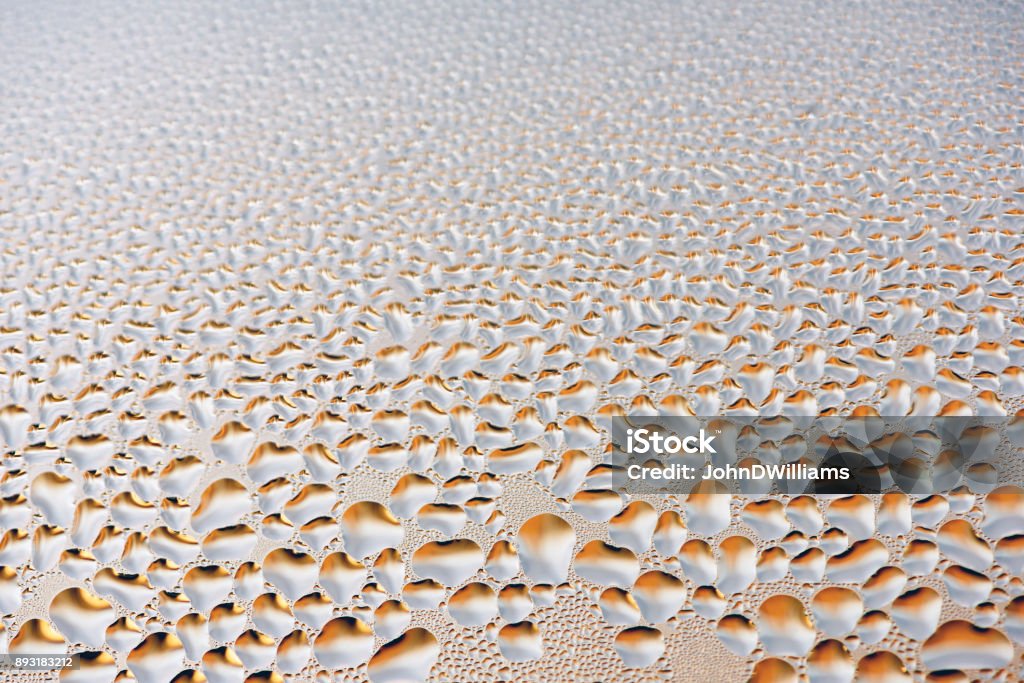 Condensation on Glass Water Droplets Background Condensation formed on glass surface of a window with silver water drops Abstract Stock Photo