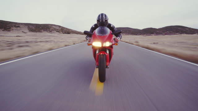 Motorcyclist riding his motorcycle down straight country road going a high speed  at sunset