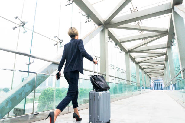 istock Businesswoman pulling wheeled suitcase walking on skywalk 893196600