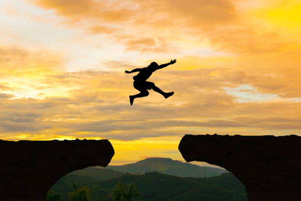 istock Man jump Mountain cliff sun light over silhouette 893196878