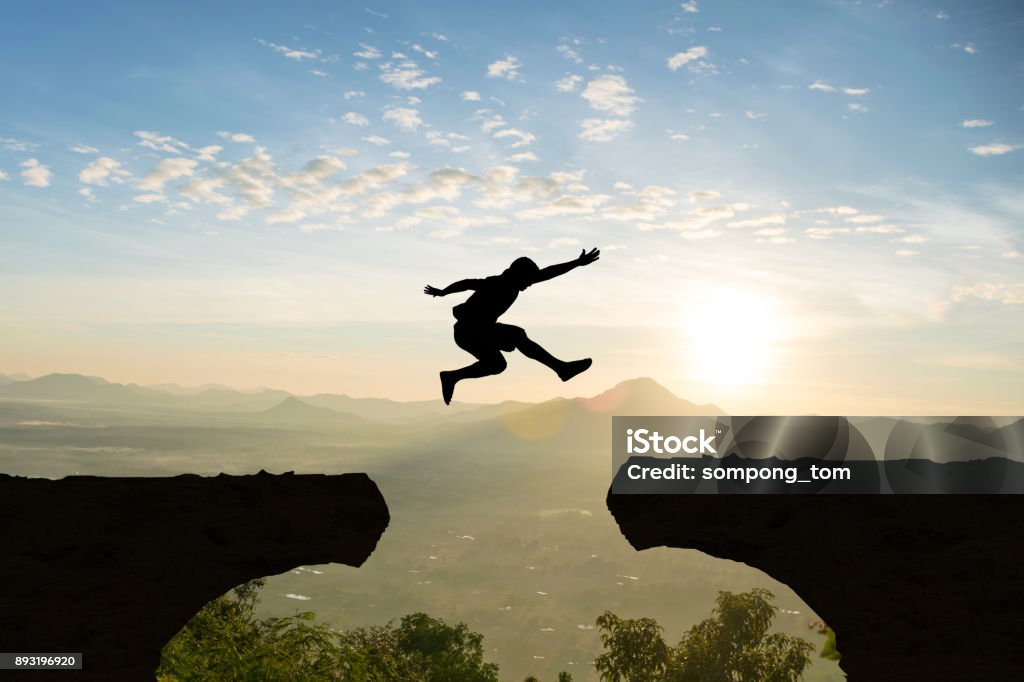 Man jump Mountain cliff sun light over silhouette Jumping Stock Photo