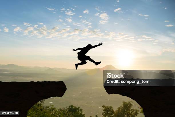 Man Jump Mountain Cliff Sun Light Over Silhouette Stock Photo - Download Image Now - Jumping, Above, Cliff