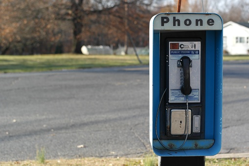 Front view of a pay phone next to an empty rural road.