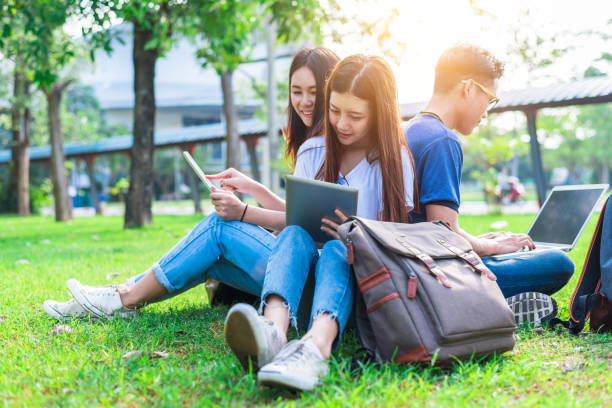 istock Group of Asian college student using tablet and laptop on grass field at outdoors. Technology and Education learning concept. Future Technology and Modern entertainment concept. Edutainment theme. 893244156