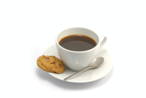 Coffee cup filled with black coffee on a white saucer with a chocolate chip cookie and spoon on a bright white background.