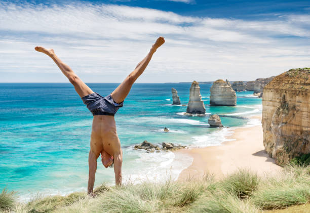 tourist doing a handstand in front of the famous twelve apostles, great ocean road, australia - beach stone wall one person imagens e fotografias de stock
