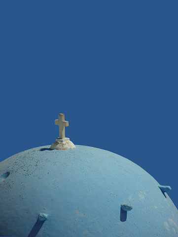 View of the national Greek flag and the top of a whitewashed Greek Orthodox Church in Ios Greece