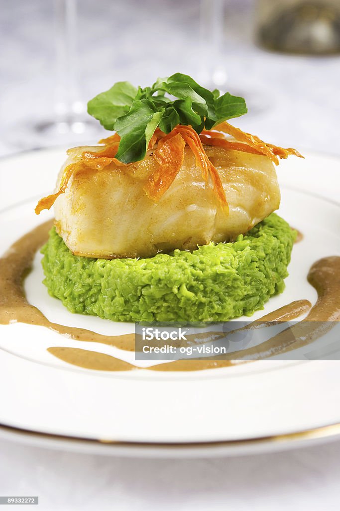 Small piece of sea bass with condiments on a white plate Chilean sea bass served with pea mash and mushroom sauce Patagonian Toothfish Stock Photo