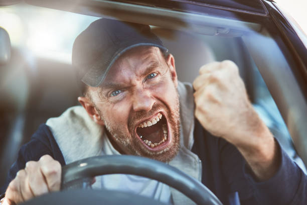 Enraged man shaking fist through windscreen: road rage A man driving loses his temper and shakes his fist, yelling, in a bout of road rage. insanity stock pictures, royalty-free photos & images