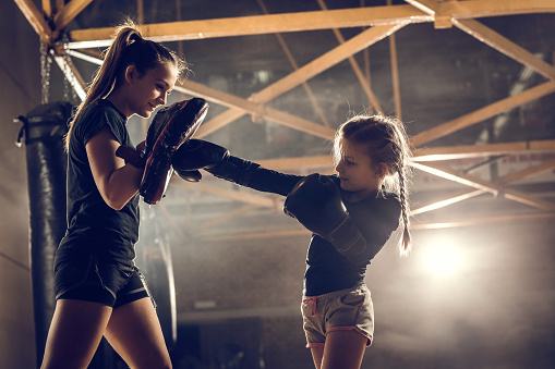 Small boxer having sports training with female instructor in a gym.