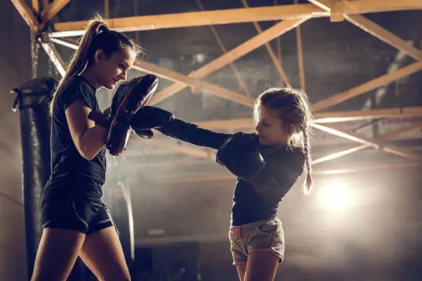 Photo of Little girl practicing boxing with her coach in health club.