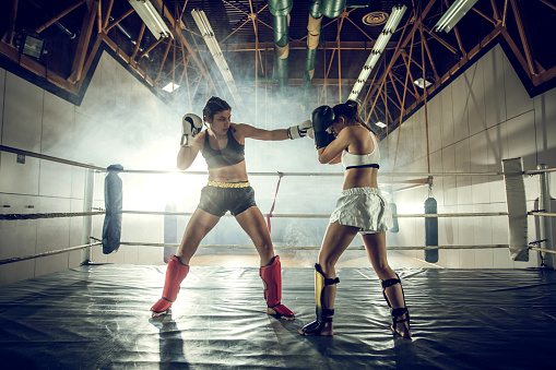 Athletic women fighting in a ring during sports training in boxing club.
