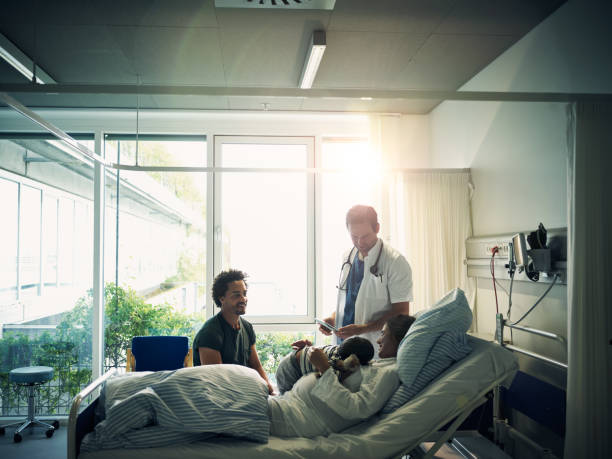 Here with you every step of the way Shot of a little boy being held by his mother who's lying on a bed while the father sits down beside them with the doctor maternity ward stock pictures, royalty-free photos & images