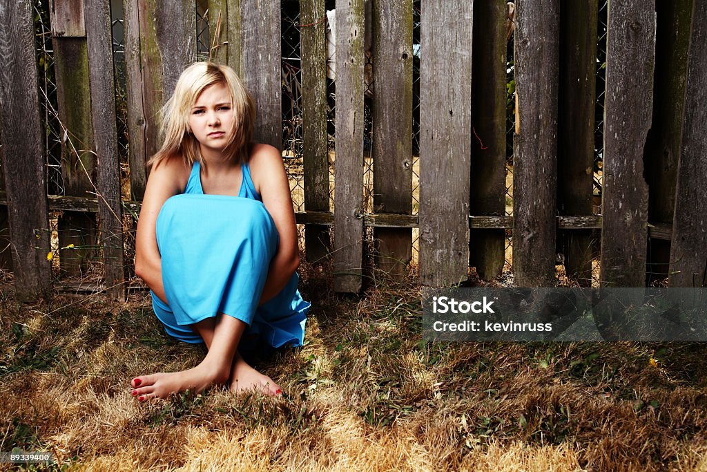 Triste giovane ragazza bionda seduta davanti a una parete - Foto stock royalty-free di Abbigliamento casual