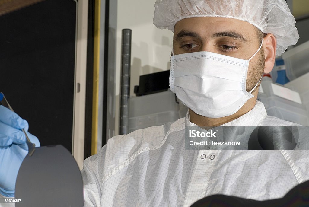Un hombre en una máscara y tapa de trabajo en una oblea de silicio. - Foto de stock de Laboratorio libre de derechos