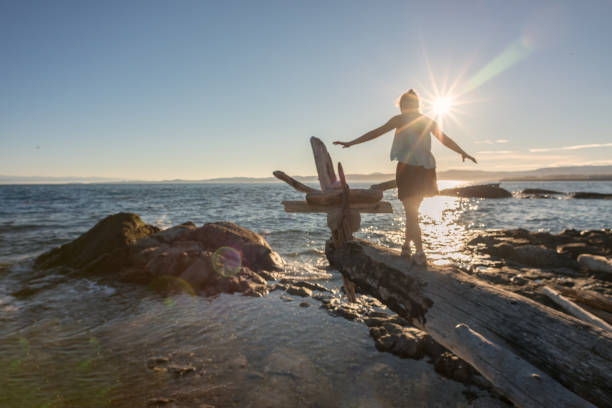 Woman Walking Along Log on Beach to Make Driftwood Sculpture