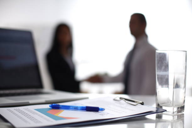 istock Laptop computer with folder on desk , two businesspeople standing in the background 893407640