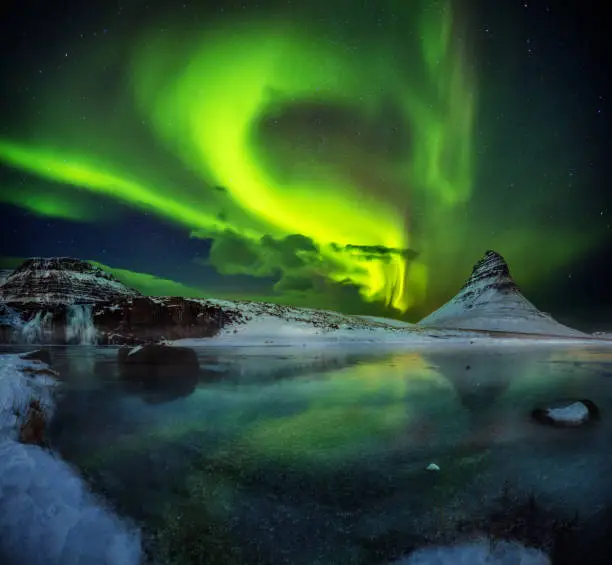 Kirkjufell mountain with beautiful aurora borealis and frozen water falls in winter, Iceland. One of the famous natural heritage in Iceland.