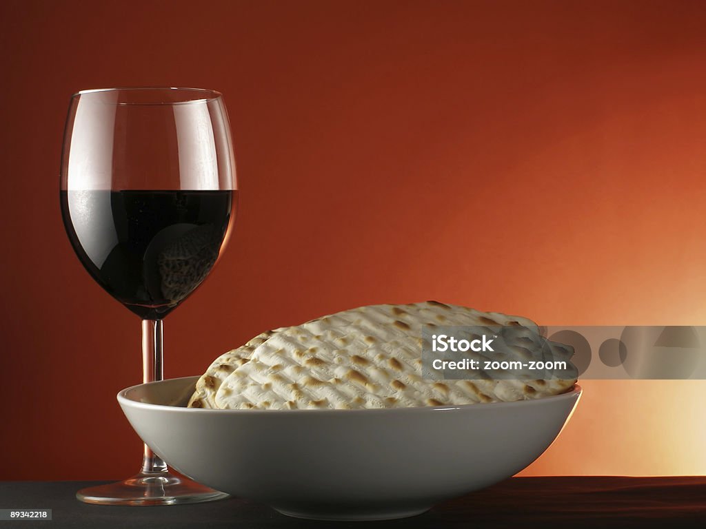 A table holding a glass of wine and a bowl of matzoh Wine and matzoh (elements of tradition jewish passover supper - seder) over red background   Alcohol - Drink Stock Photo