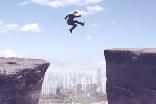 istock American businessman jumping through gap cliff 893423376