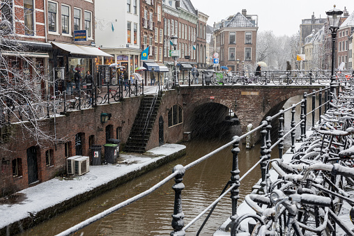 Utrecht: canals with trees, shops and a bridge in Utrecht in a winter snow storm, Netherlands.