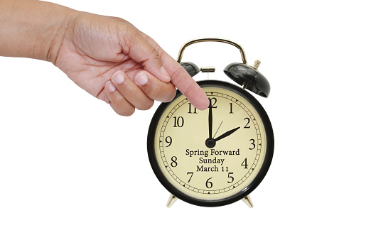 Hand pointing to hour hand on Spring Forward Daylight Savings March 11 Alarm clock white background