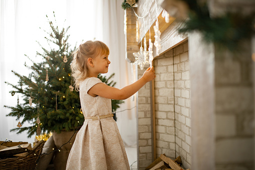 Little child girl in dress are decorating room with Christmas decorations.