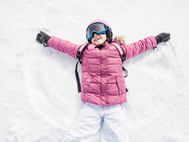 little girl laughing and playing snow angel - snow gear imagens e fotografias de stock