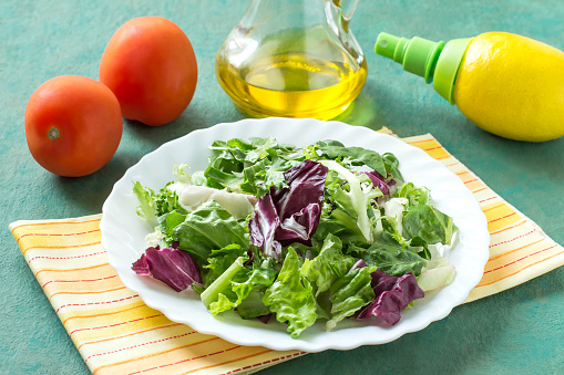Ingredients for preparation of vitamin salad: different salad leaves, tomatoes, olive oil, lemon with spray pump. Healthy food and vitamins