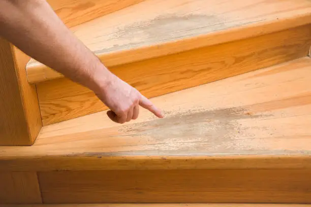Photo of Man's hand pointing to the old scratched wooden stairs' step in the house. Problems and solutions concept.