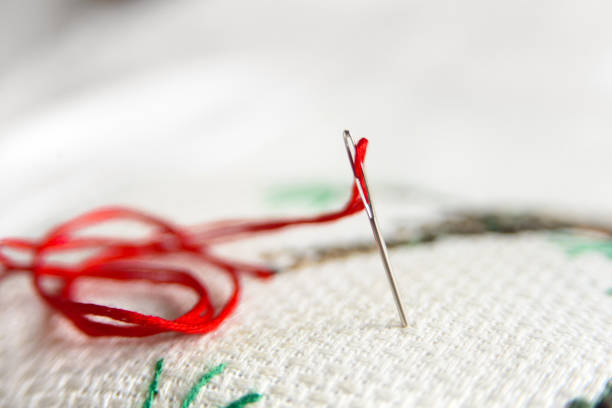 istock Cross-stitch embroidery and needle with red thread. Embroidery macro close up. View from above. Free copy space. 893481814