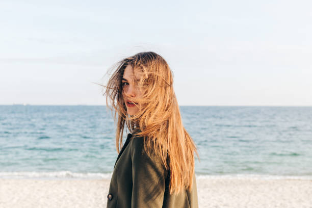 Beautiful young woman with long brown hair Beautiful young woman with long brown hair turns and looks at camera on the beach turning back stock pictures, royalty-free photos & images