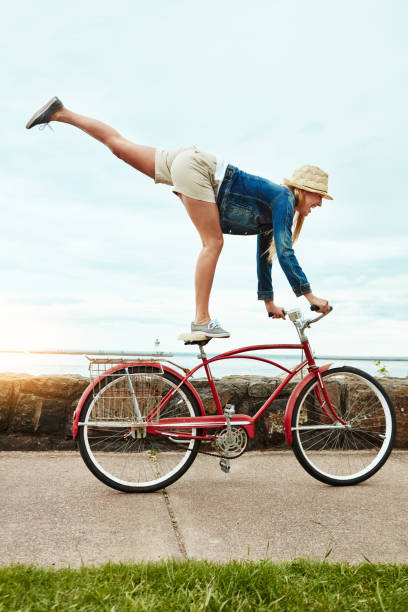 If everyone could see me now Shot of a cheerful young woman riding her bicycle down a street while performing tricks outside during the day bicycle stunts stock pictures, royalty-free photos & images