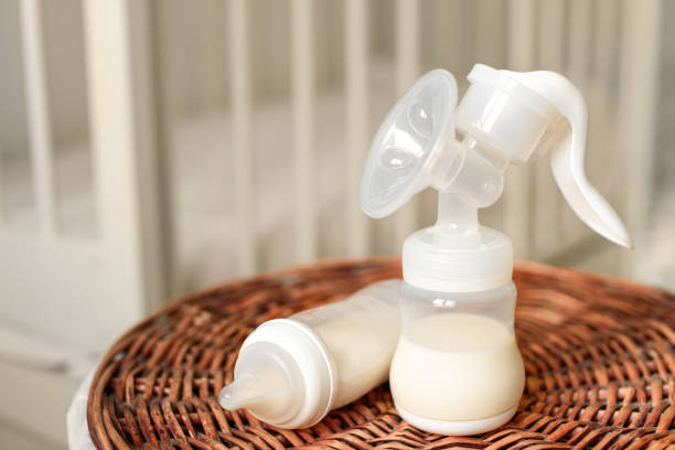 Breast pump and bottle with milk for baby on a straw basket. Kids room with a bed. Breast pump and bottle with milk for baby on a straw basket. Kids room with a bed. breast milk stock pictures, royalty-free photos & images