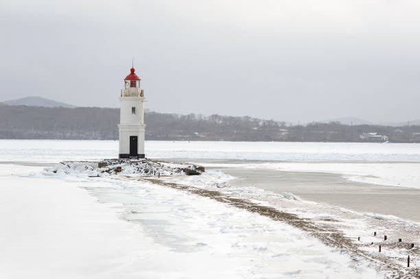 istock Red and white lighthouse at winter snowy sea coast. 893521926