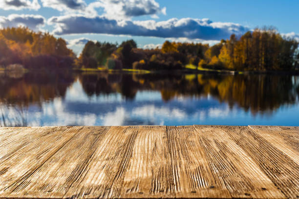 istock Empty rustic wood table top on  blurred colorful autumn landscape background with fall forest and blue sky with cloudscape reflection on the lake. Can montage or display your products 893525330