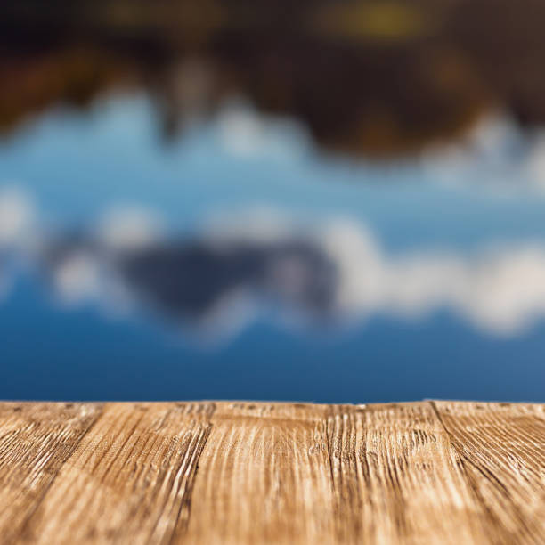 istock Empty rustic wood table top on  blurred colorful autumn landscape background with fall forest and blue sky with cloudscape reflection on the lake. Can montage or display your products 893525488