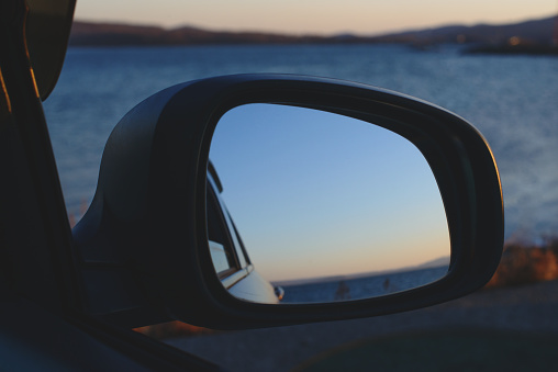 Reflection of the sunset in the sea in a car side view mirror.