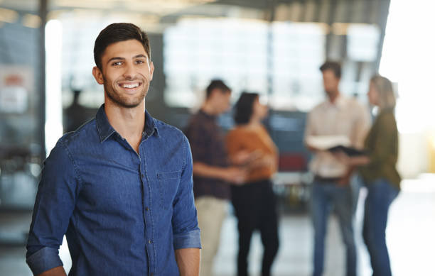 He’s got exceptional creative talents to boast Portrait of a young designer standing in an office with his colleagues in the background incidental people photos stock pictures, royalty-free photos & images