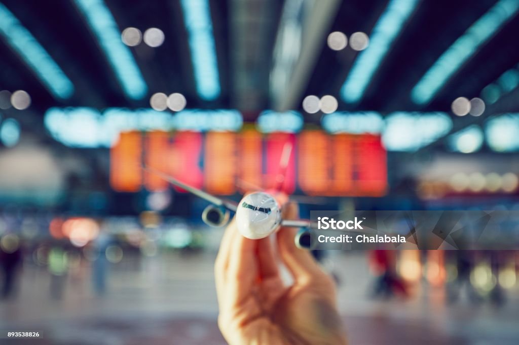 Hand is holding model airplan Hand is holding model airplane against arrival and departure board in a airport terminal. Model Airplane Stock Photo