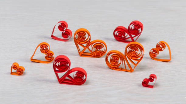 Handmade red and orange paper hearts in quilling technique on light wooden background. Close shot. Ratio 16:9. stock photo