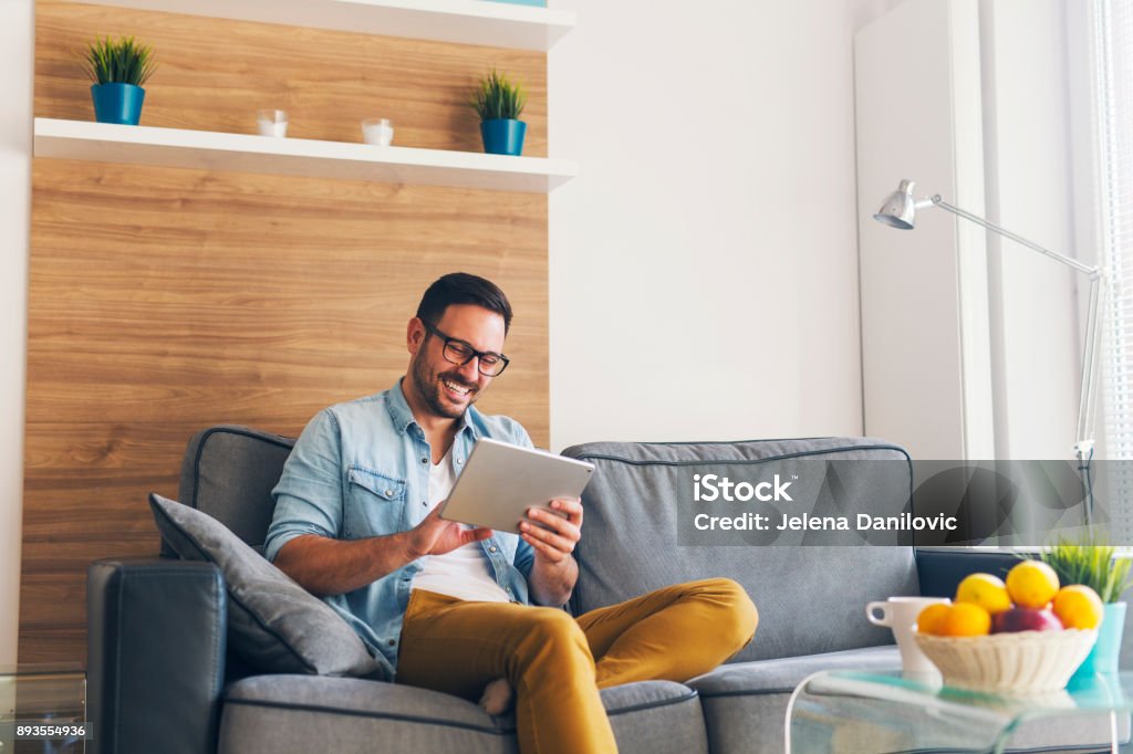 Leisure Smiling young man relaxing and using tablet on couch Men Stock Photo