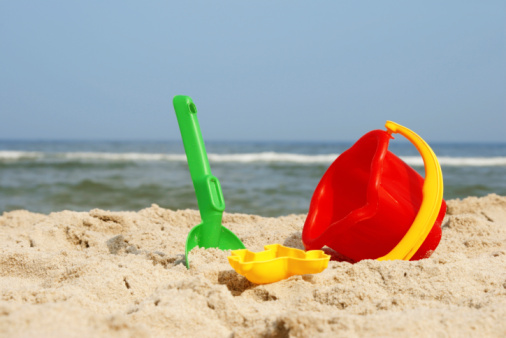 Children's bucket and shovel, castle of sand on the sand beach on a sunny day. Toys for kid play on the sea side. Travel on the beach concept. Vacation concept. Children games in the sand