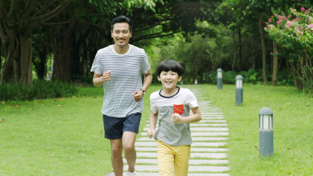 Asian father runing together with his little son in park in summer stock photo