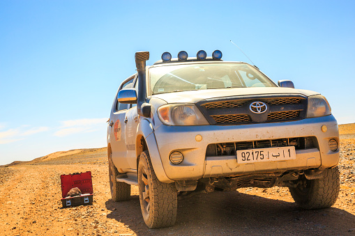 Ait Saoun, Morocco - February 23, 2016: Front view of a 4x4 driverless assistance vehicle in the Moroccan desert under a beautiful blue sky. We can see a toolbox placed right next to the vehicle on the sand.
