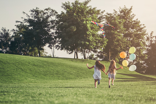 Little pretty girls having fun outdoor. Two cute girls are running on green grass with air balloons. Best friends