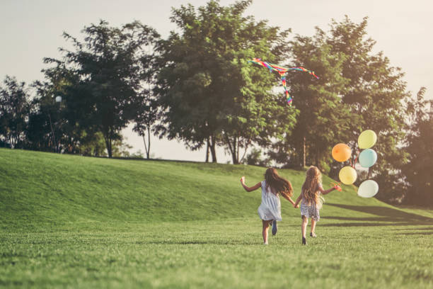 Children having fun. Little pretty girls having fun outdoor. Two cute girls are running on green grass with air balloons. Best friends natural parkland stock pictures, royalty-free photos & images