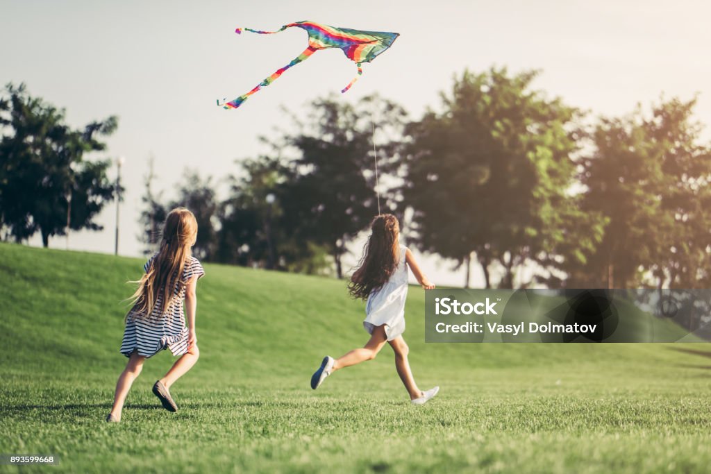 Children having fun. Little pretty girls having fun outdoor. Two cute girls are running on green grass with kite. Best friends. Family Stock Photo