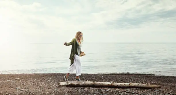 Shot of a young woman walking along a log at a lake